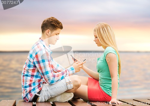 Image of couple with smartphones sitting on bench