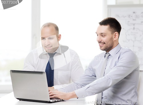 Image of two smiling businessmen with laptop in office