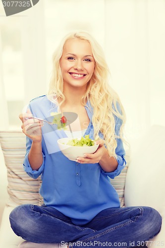 Image of smiling young woman with green salad at home