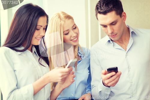 Image of smiling business team with smartphones in office