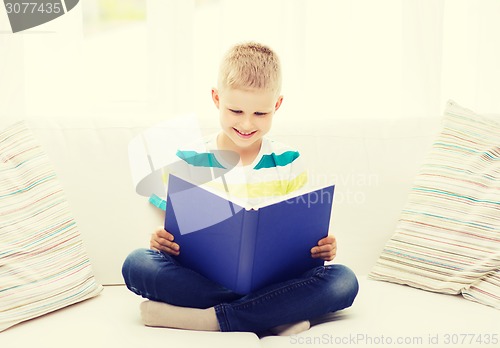 Image of smiling little boy reading book on couch