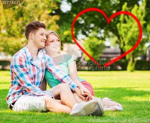 Image of smiling couple sitting on grass in summer park