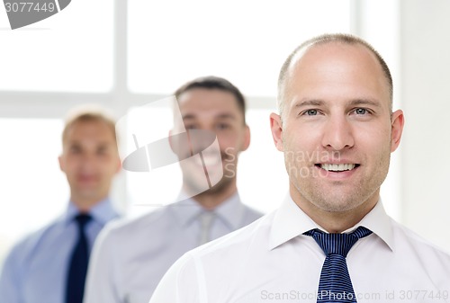 Image of smiling businessman in office with team on back