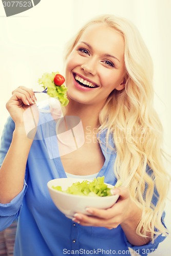Image of smiling young woman with green salad at home