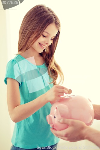 Image of smiling little girl putting coin into piggy bank