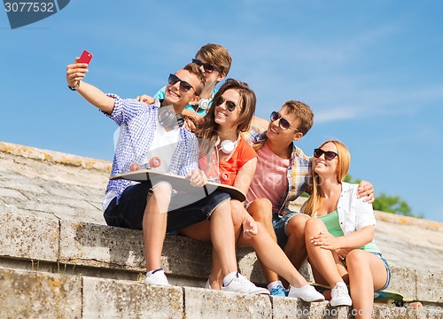Image of group of smiling friends with smartphone outdoors