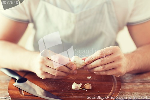 Image of male hands taking off peel of garlic on board