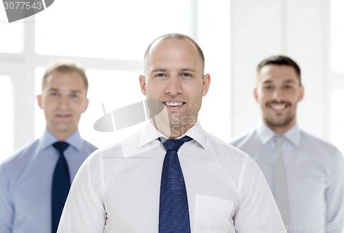 Image of smiling businessman in office with team on back