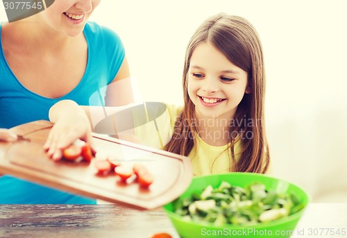 Image of little girl with mother adding tomatoes to salad