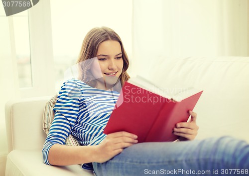 Image of smiling teenage girl reading book on couch