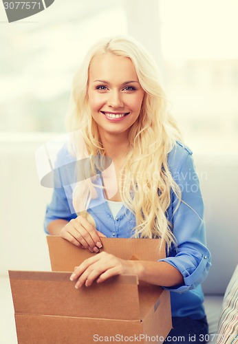 Image of smiling young woman opening cardboard box at home