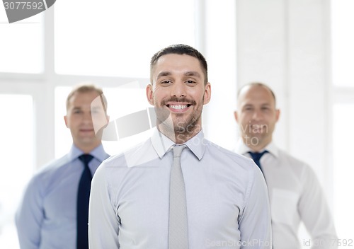 Image of smiling businessman in office with team on back