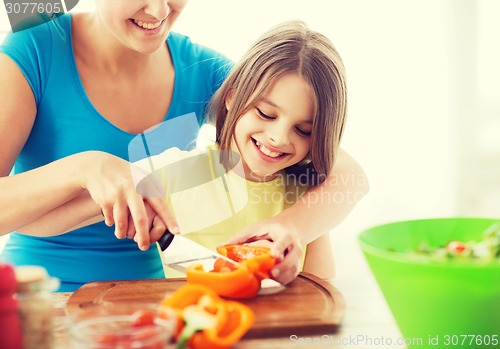 Image of smiling little girl with mother chopping pepper