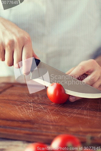 Image of male hand cutting tomato on board with knife