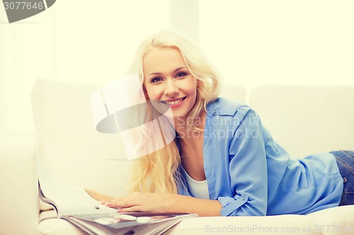 Image of woman lying on couch and reading magazine at home