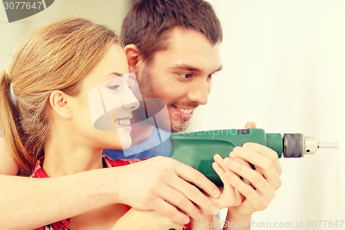 Image of smiling couple drilling hole in wall at home