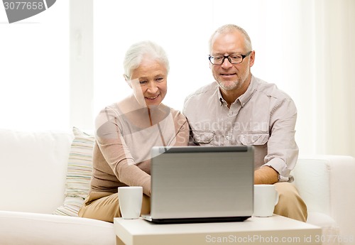 Image of happy senior couple with laptop and cups at home