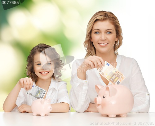 Image of mother and daughter putting money to piggy banks