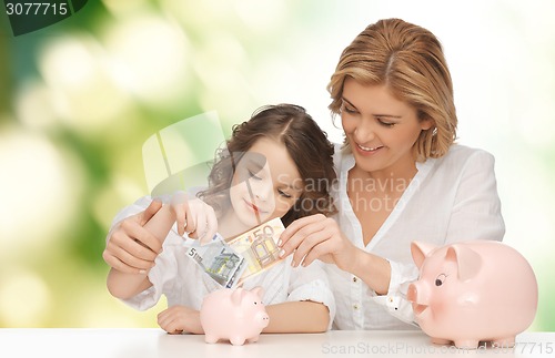 Image of mother and daughter putting money to piggy banks