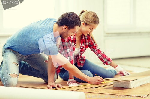 Image of smiling couple measuring wood flooring