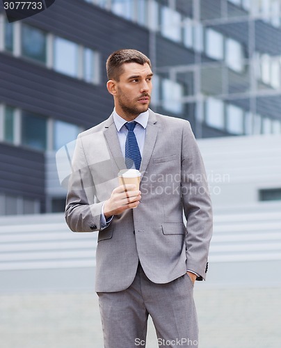 Image of young serious businessman with paper cup outdoors
