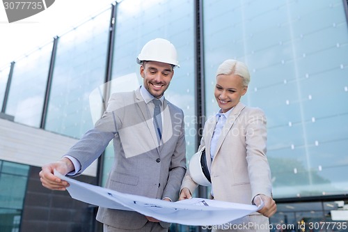 Image of smiling businessmen with blueprint and helmets