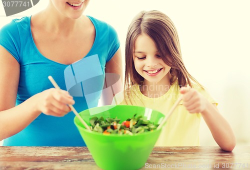 Image of little girl with mother mixing salad in kitchen