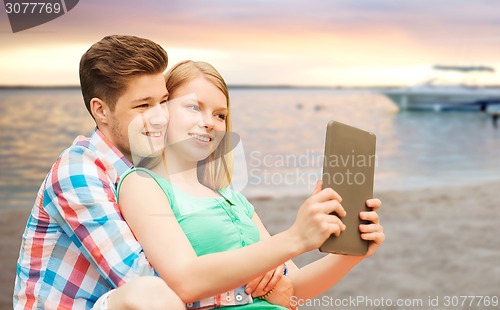 Image of couple with tablet pc taking selfie over beach