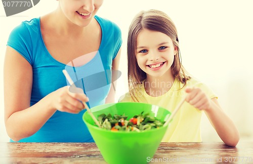 Image of little girl with mother mixing salad in kitchen