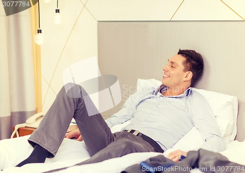 Image of happy businesswoman lying in bed in hotel room