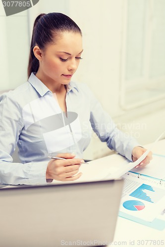 Image of businesswoman with laptop and charts in office