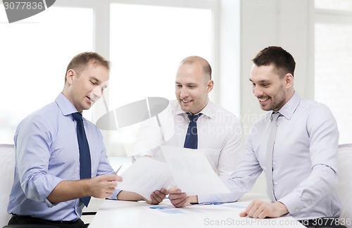 Image of smiling businessmen with papers in office
