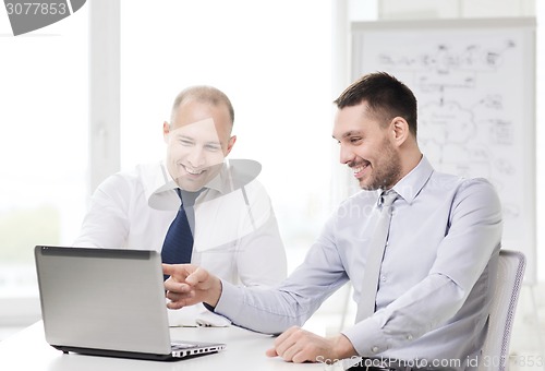 Image of two smiling businessmen with laptop in office