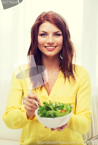 Image of smiling young woman with green salad at home