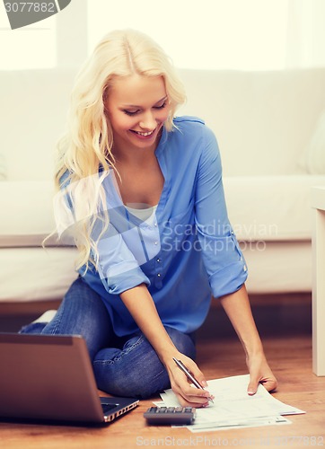 Image of smiling woman with papers, laptop and calculator