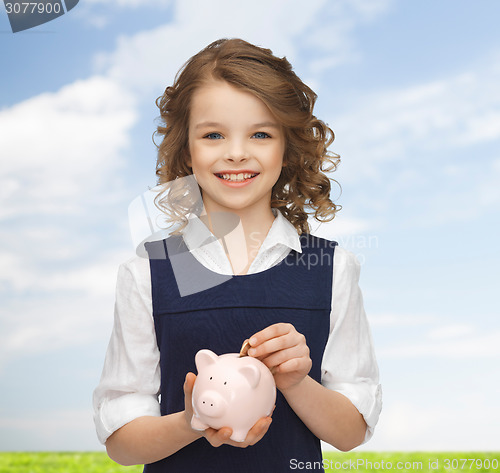 Image of smiling girl putting coin into piggy bank