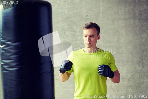 Image of young man in gloves boxing with punching bag