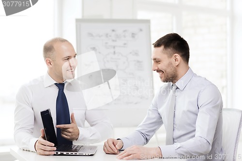 Image of two smiling businessmen with laptop in office
