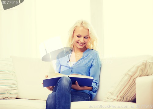 Image of smiling woman reading book and sitting on couch