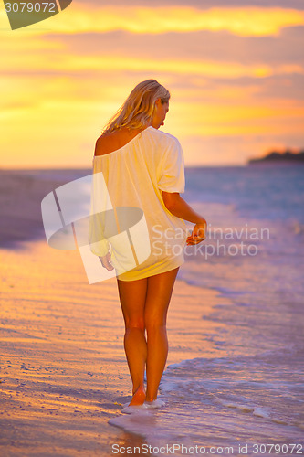 Image of Lady on sandy tropical beach at sunset.