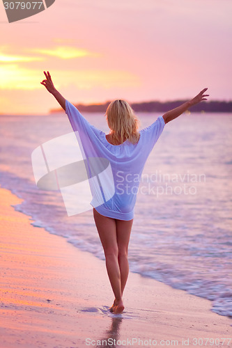 Image of Lady on sandy tropical beach at sunset.