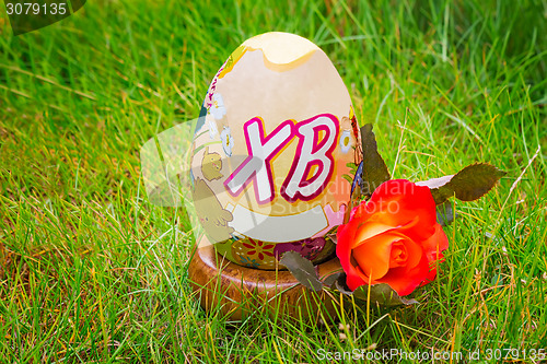 Image of Easter egg and flower rose among the green grass.