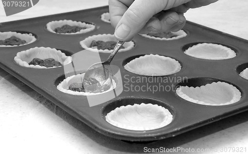 Image of A woman's hand holding a teaspoon as she fills jam tarts