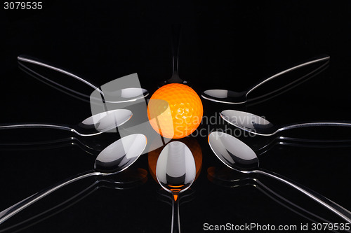 Image of Teaspoons and orange golf ball on the black glass table 