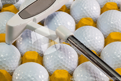 Image of White golf balls in the yellow box and golf putter