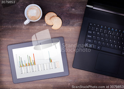 Image of Tablet touch computer gadget on wooden table, graph