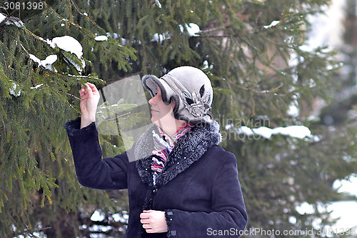 Image of The woman in a hat and a sheepskin coat costs near a fir-tree in