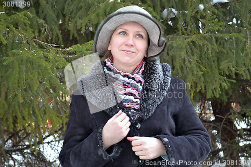 Image of The woman in a hat and a sheepskin coat costs near a fir-tree in