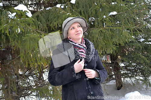 Image of The woman in a hat and a sheepskin coat costs near a fir-tree in