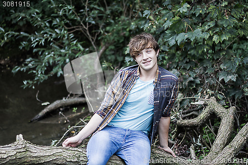 Image of young man sitting on branch over a stream